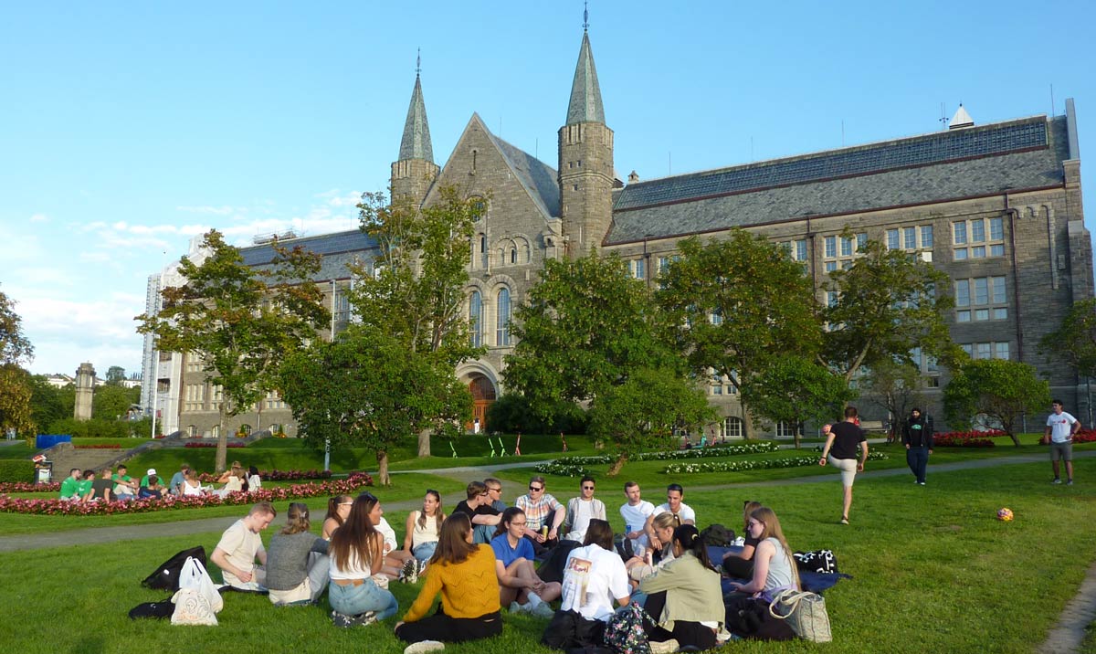 Students sitting on the grass in front of Gløshaugen. Photo